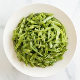 A white bowl on a marble surface, filled with French green beans.