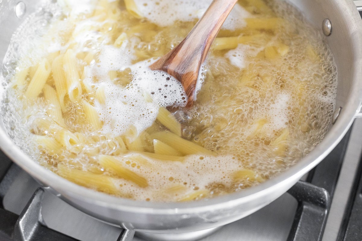 Penne pasta cooking in a stainless steel pan.