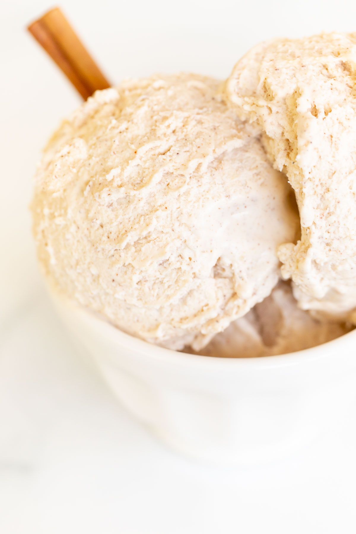 A white bowl full of homemade cinnamon ice cream with a cinnamon stick as garnish on the side