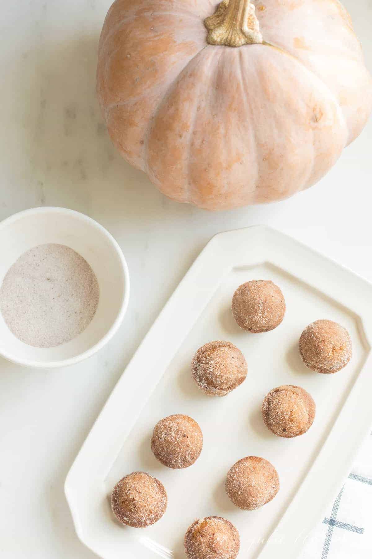 pumpkin muffins on a white platter, with a pale peach real pumpkin in the background