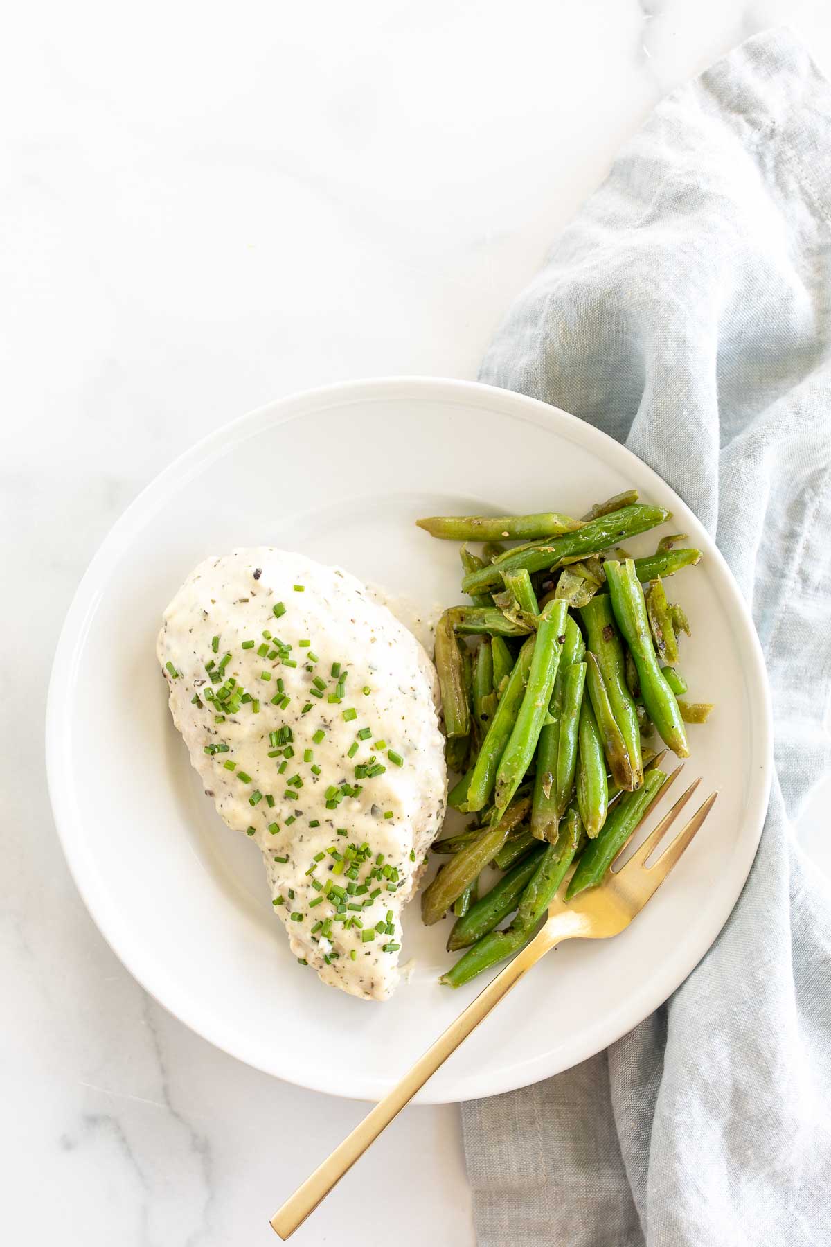 A white plate of chicken and vegetables with a gold fork. 