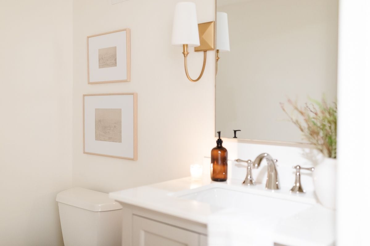 A small bathroom with gold sconces and walls painted Cloud White