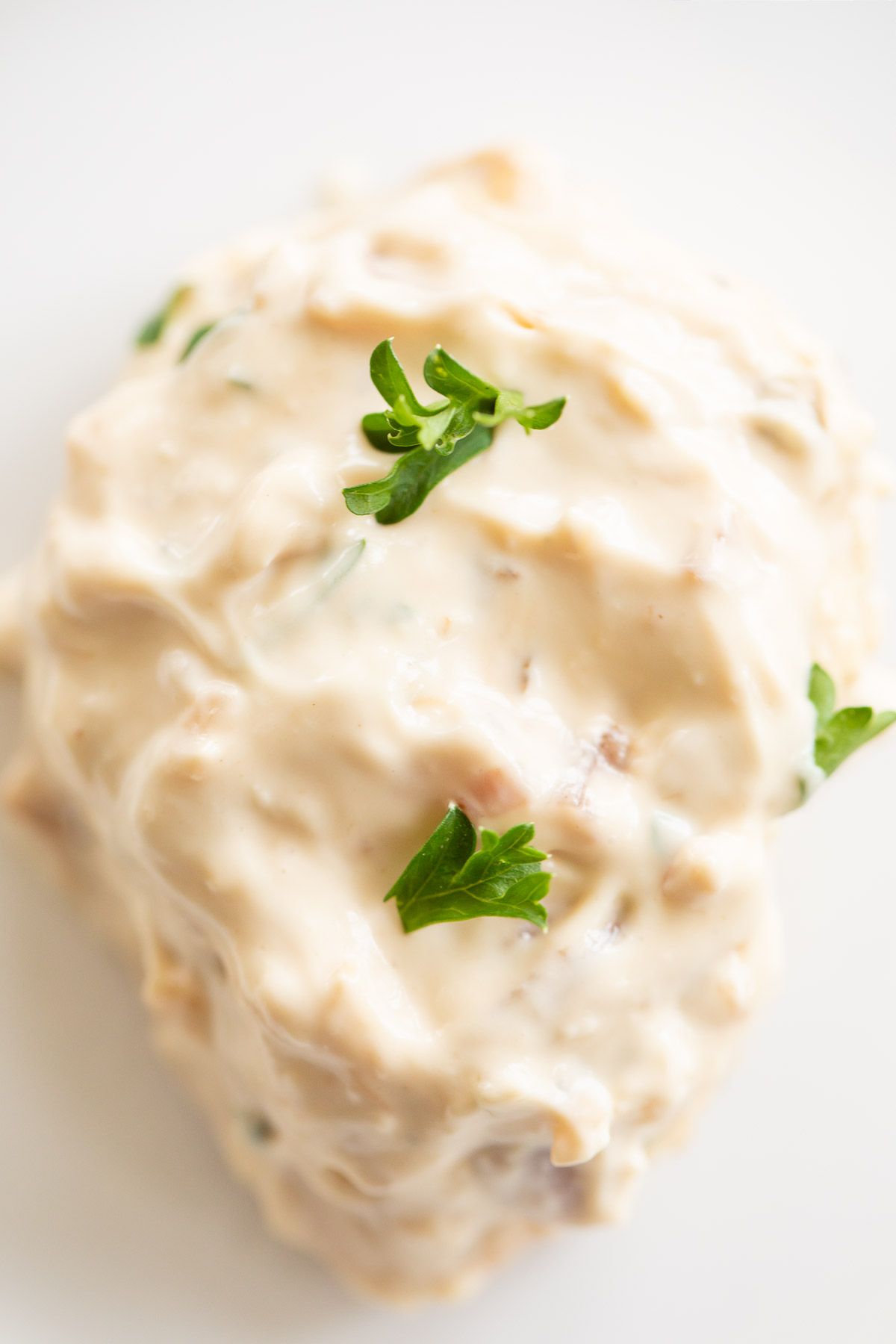 A cream cheese chicken breast with chopped parsley on a white plate
