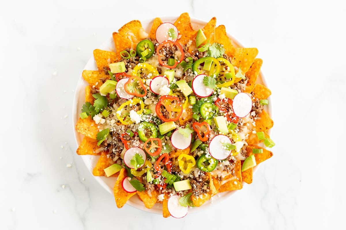 A white plate full of Doritos nachos, on a marble surface.