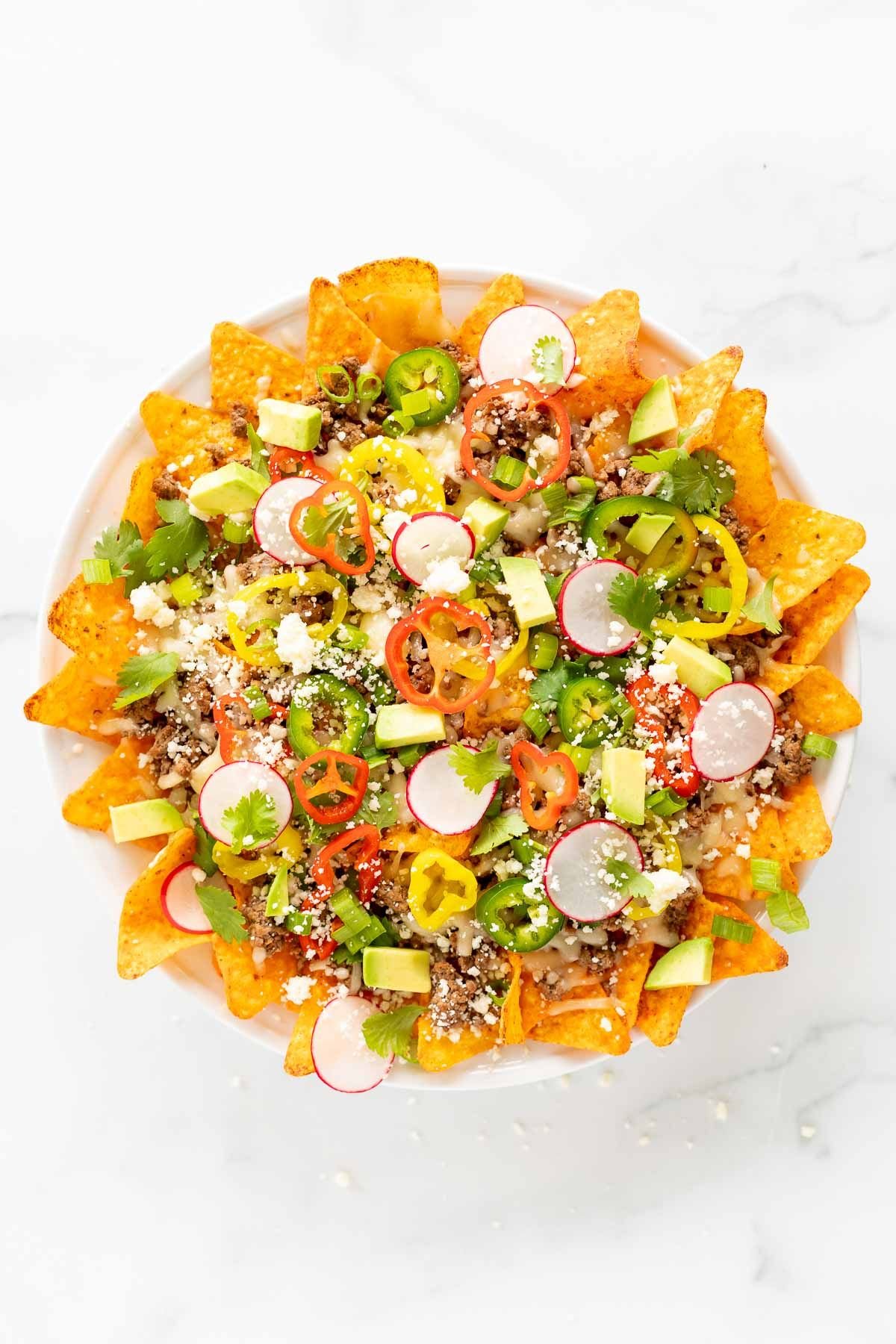 A white plate full of Doritos nachos, on a marble surface.