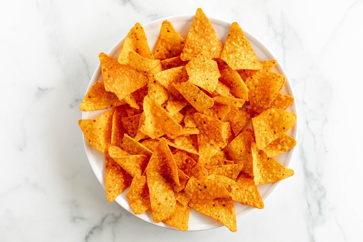 A white plate full of Doritos, on a marble surface.