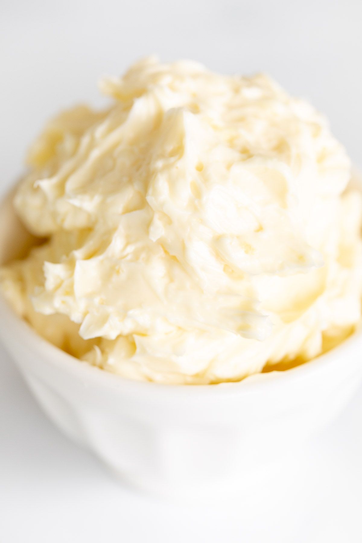 A small white bowl of garlic butter on a marble surface.