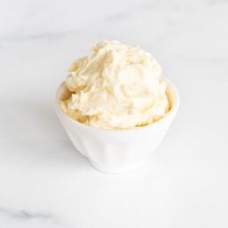 A small white bowl of garlic butter on a marble surface.