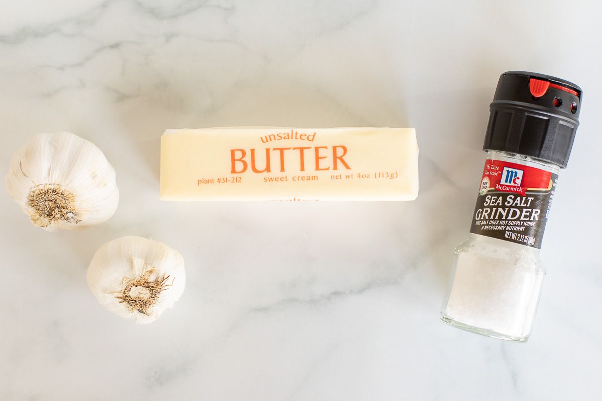 Garlic cloves, a stick of butter and a sea salt grinder on a marble surface