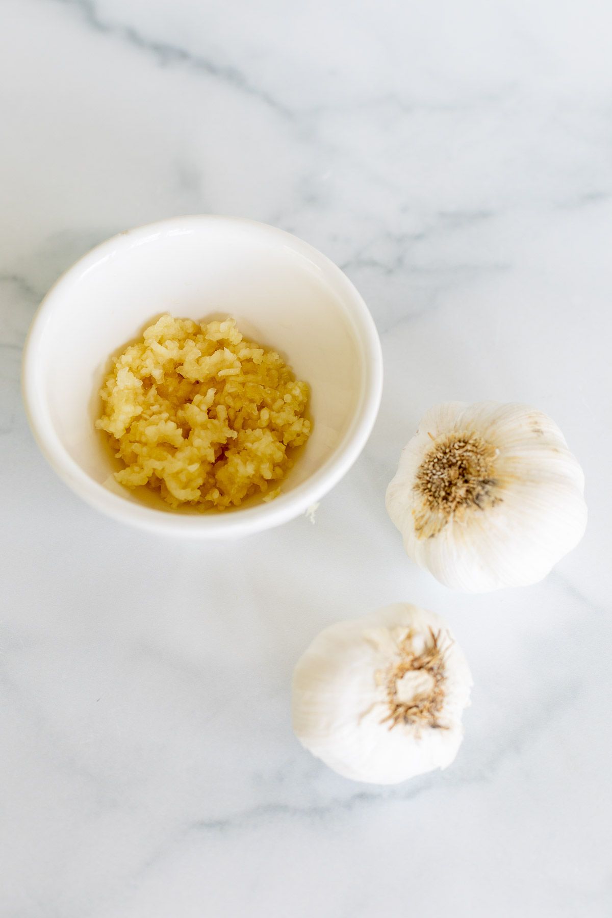 A bowl of fresh minced garlic with garlic cloves to the side