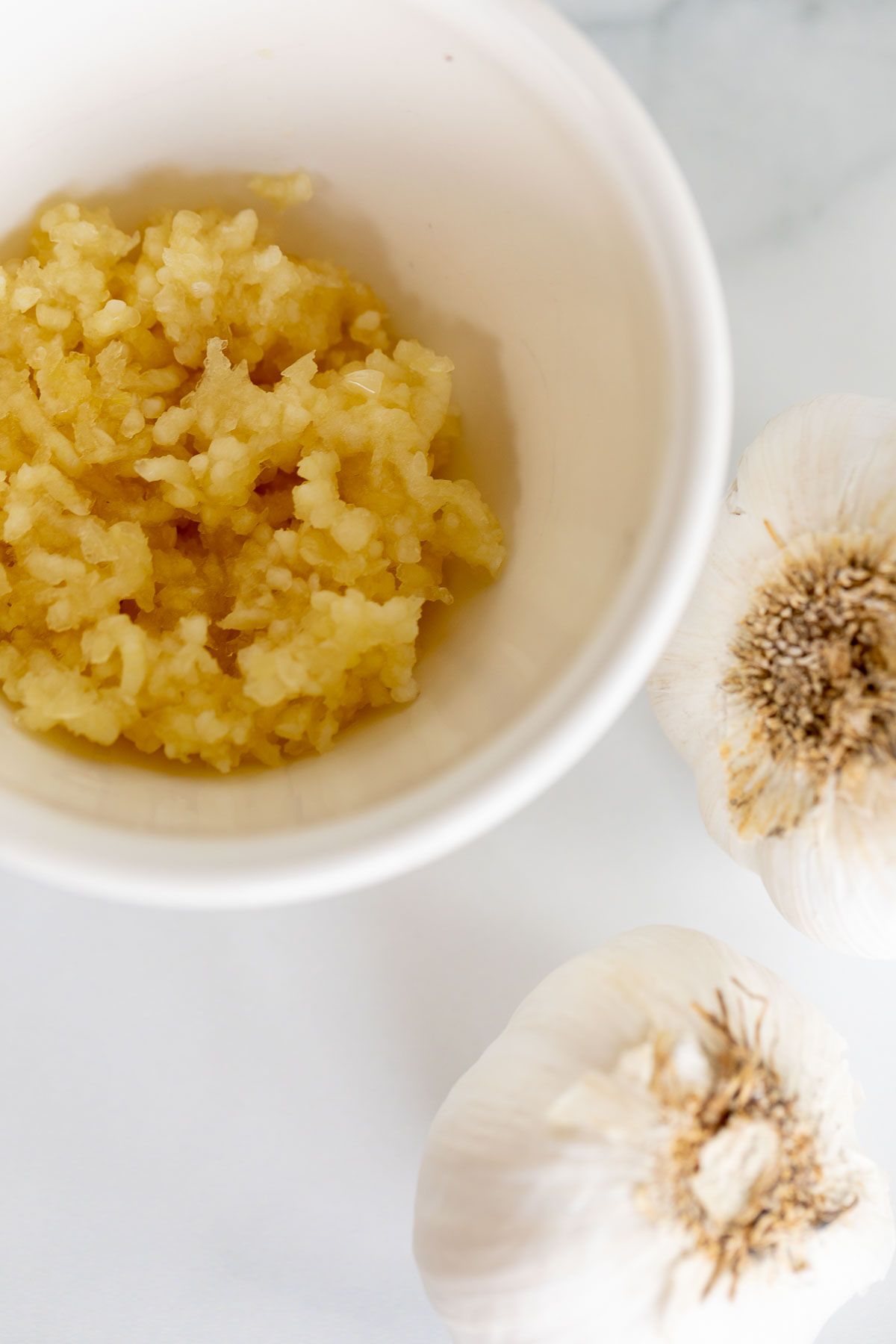 A bowl of fresh minced garlic with garlic cloves to the side