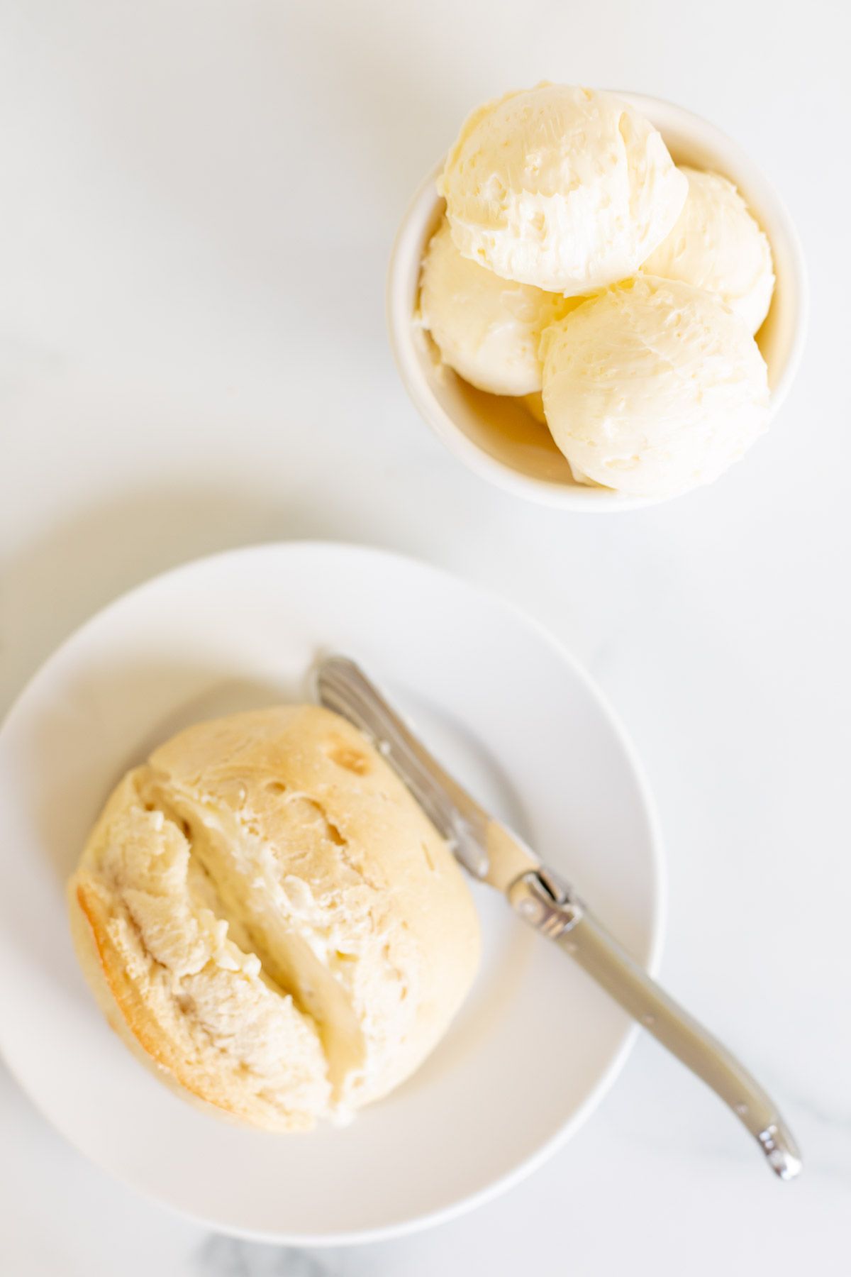 A dinner roll on a white plate with a bowl of garlic butter to the side.