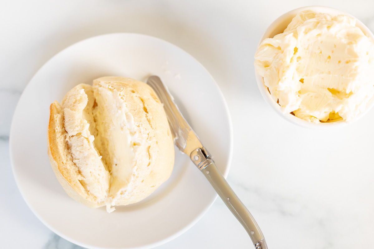 A dinner roll on a white plate with a bowl of garlic butter to the side.