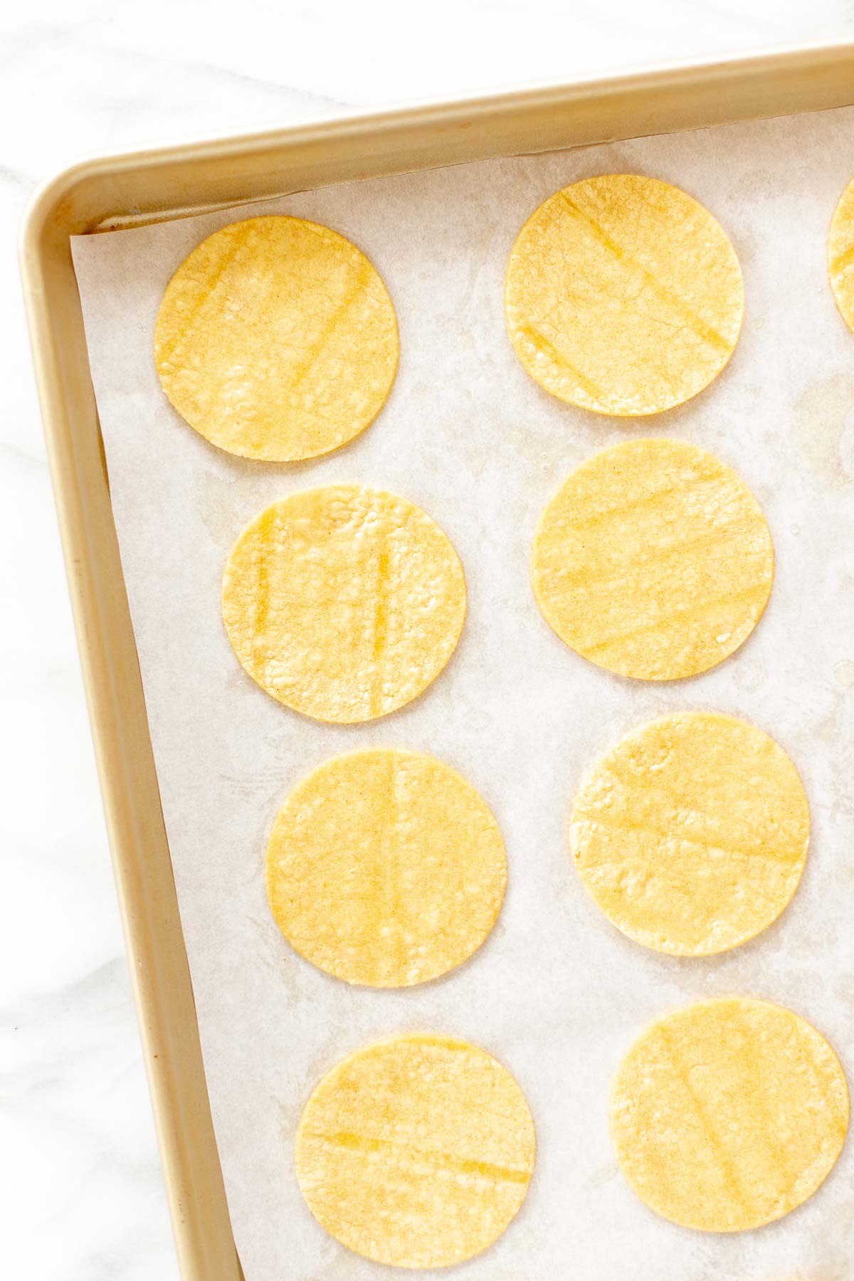 Mini corn tortillas on a gold baking sheet.