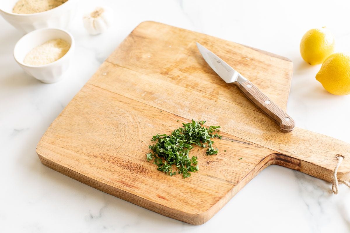 A wooden cutting board with chopped parsley and a knife.