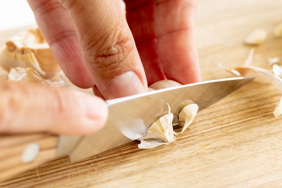 A hand cutting a bulb of garlic on a wooden cutting board