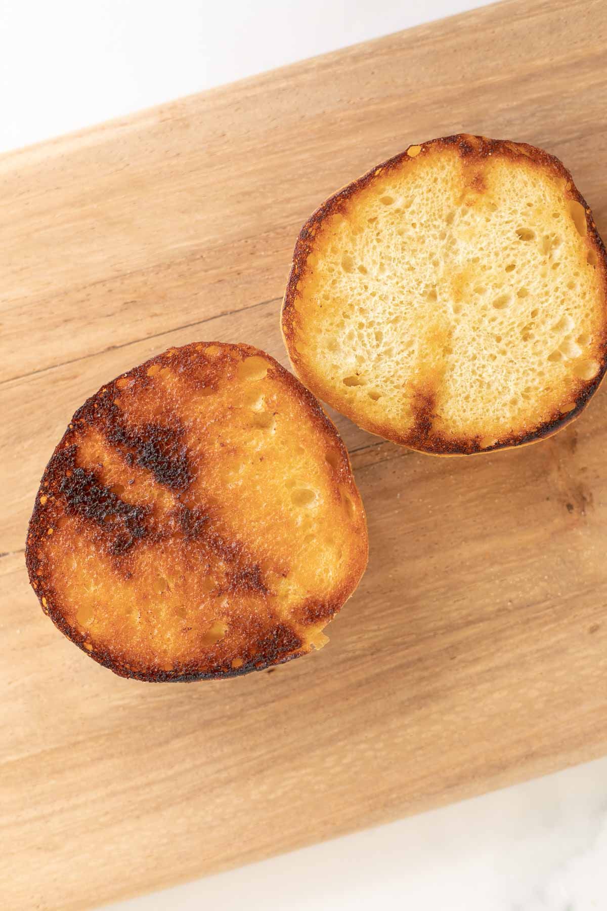 A toasted burger bun on a wooden cutting board