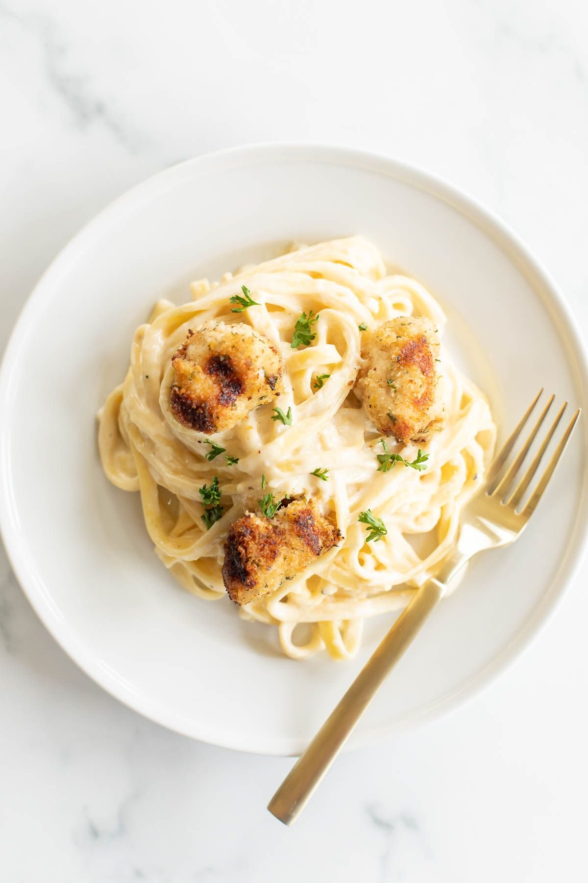 A white plate with fettuccine alfredo topped with spiedini.