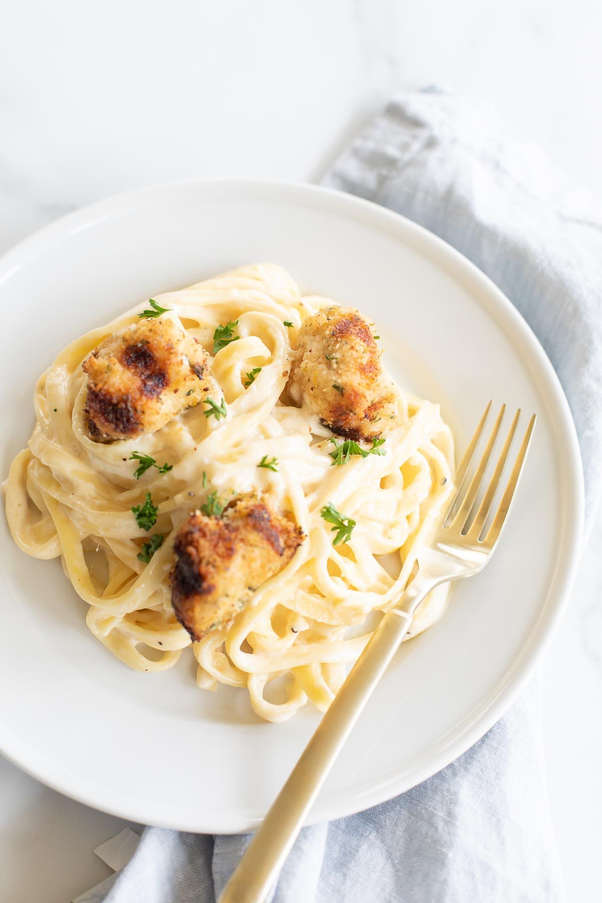 A white plate with fettuccine alfredo topped with spiedini.