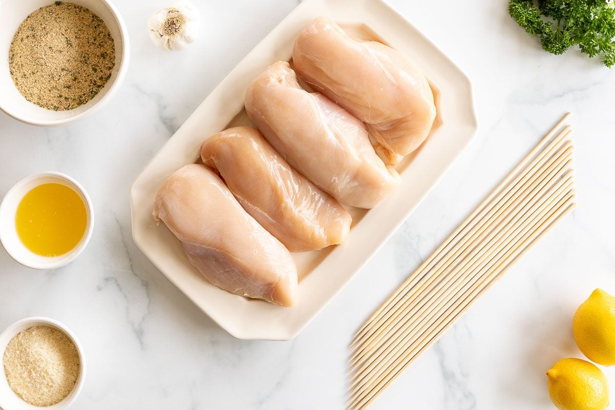 Spiedini ingredients laid out on a white surface, chicken breasts in the center.