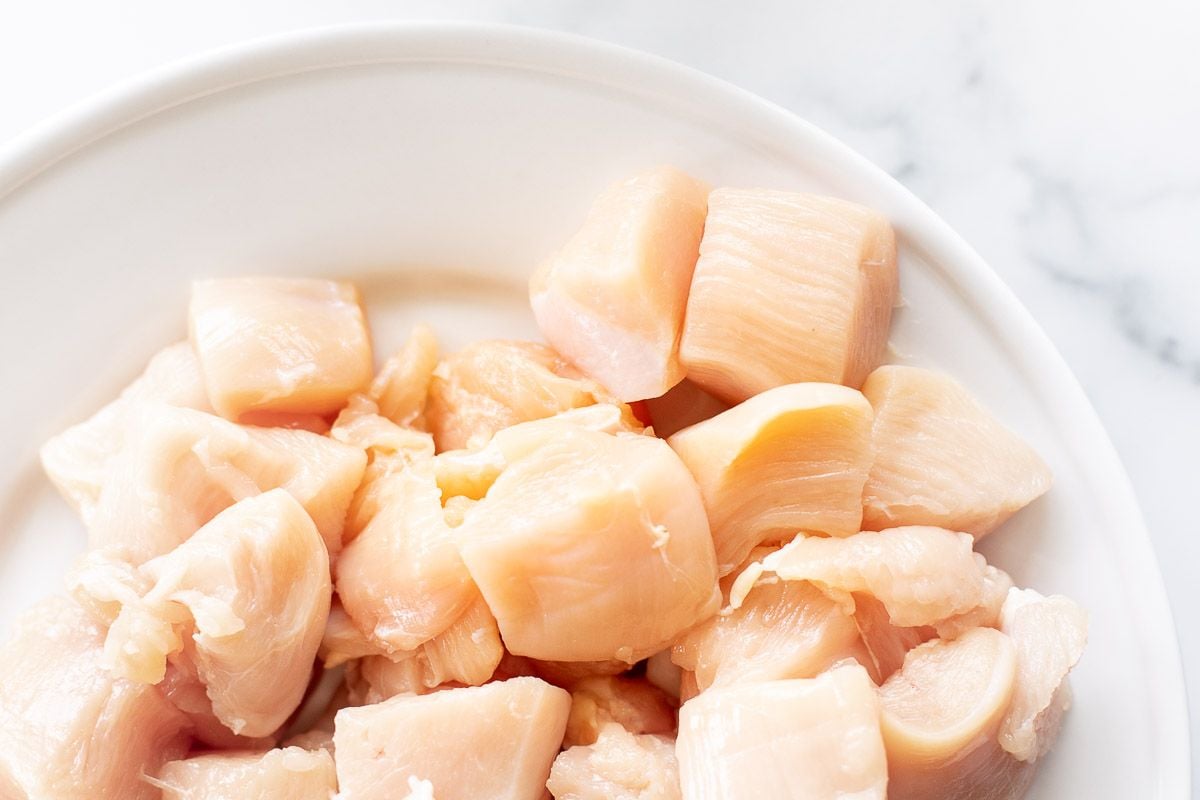 Chunks of uncooked chicken on a white plate.