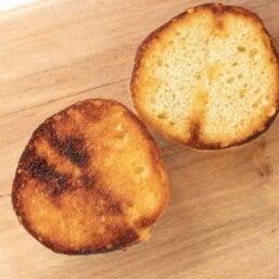 A toasted burger bun on a wooden cutting board