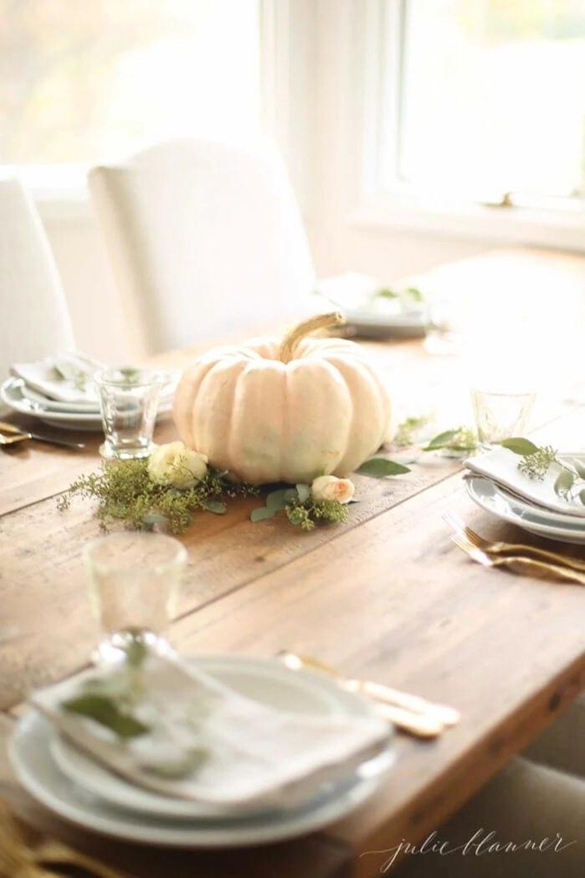 A Thanksgiving table setting with a pumpkin centerpiece and greenery.