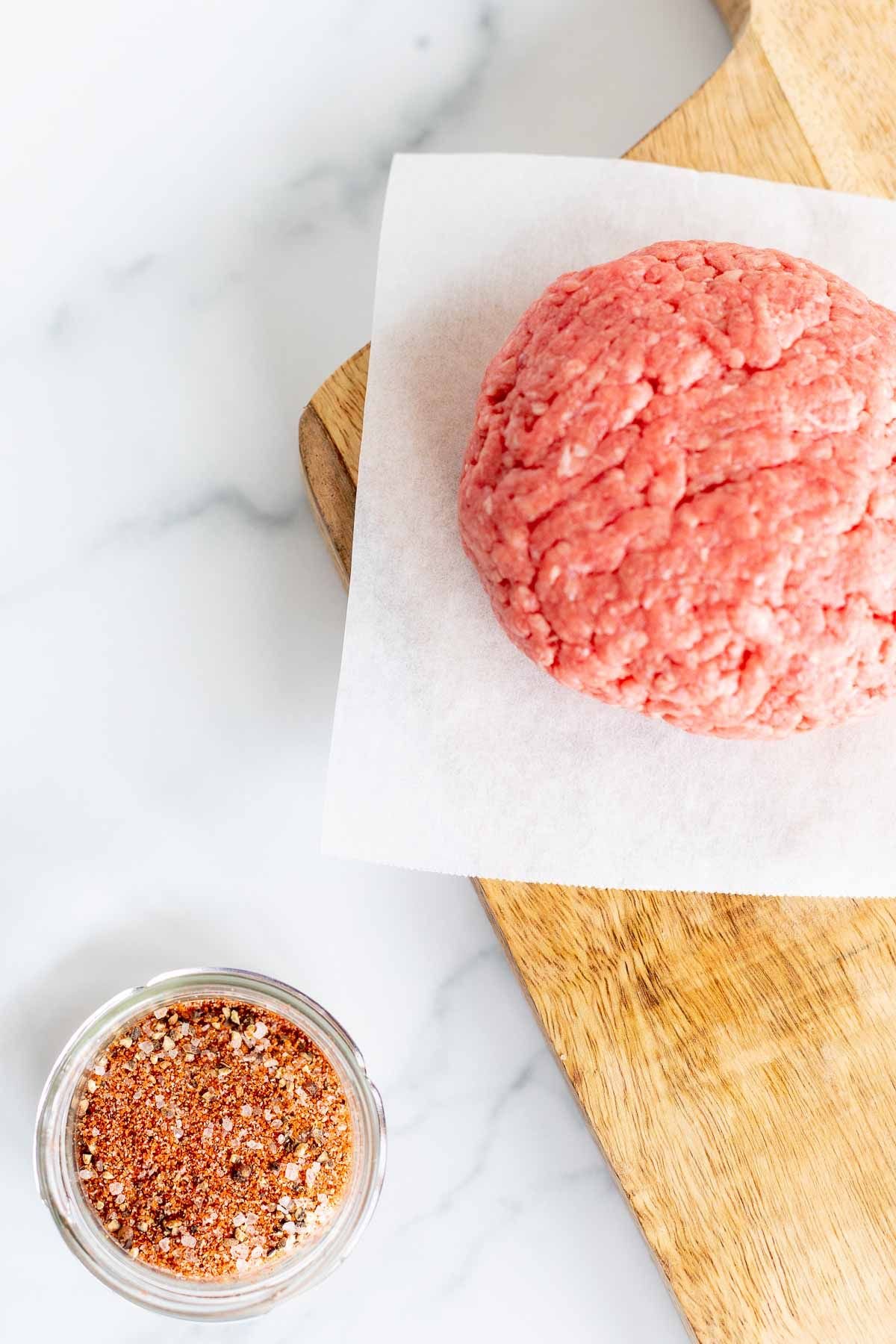 A small glass bowl of burger seasoning, with an uncooked burger patty to the side