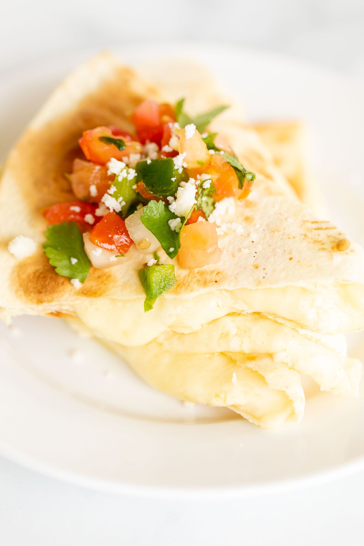 Cheese quesadilla sliced and stacked on a white plate, topped with pico de gallo