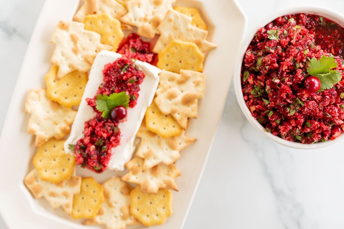 A platter of crackers surrounding cranberry salsa on a block of cream cheese