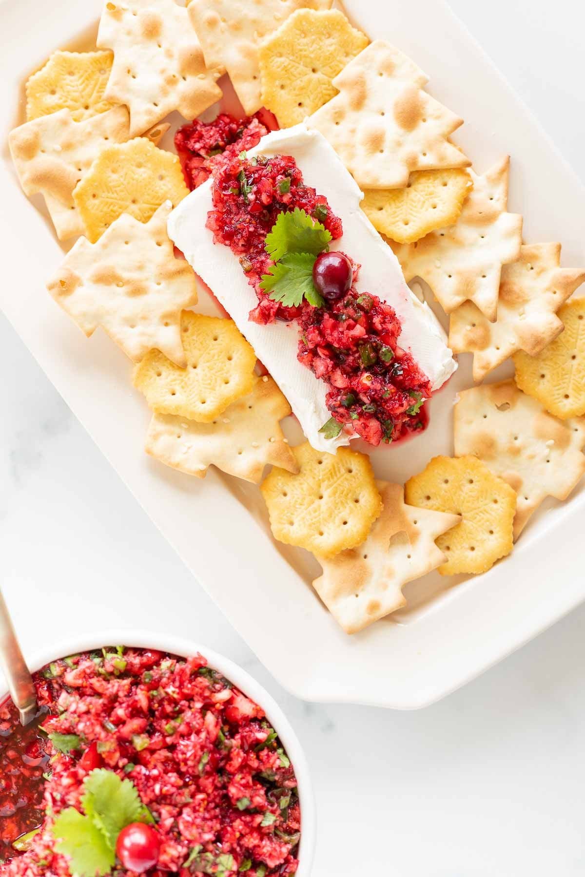 A platter of crackers surrounding cranberry salsa on a block of cream cheese