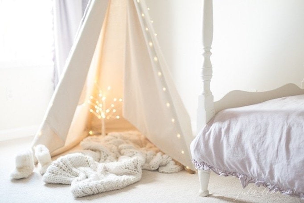 A teepee adorned with fairy lights in a girl's bedroom.