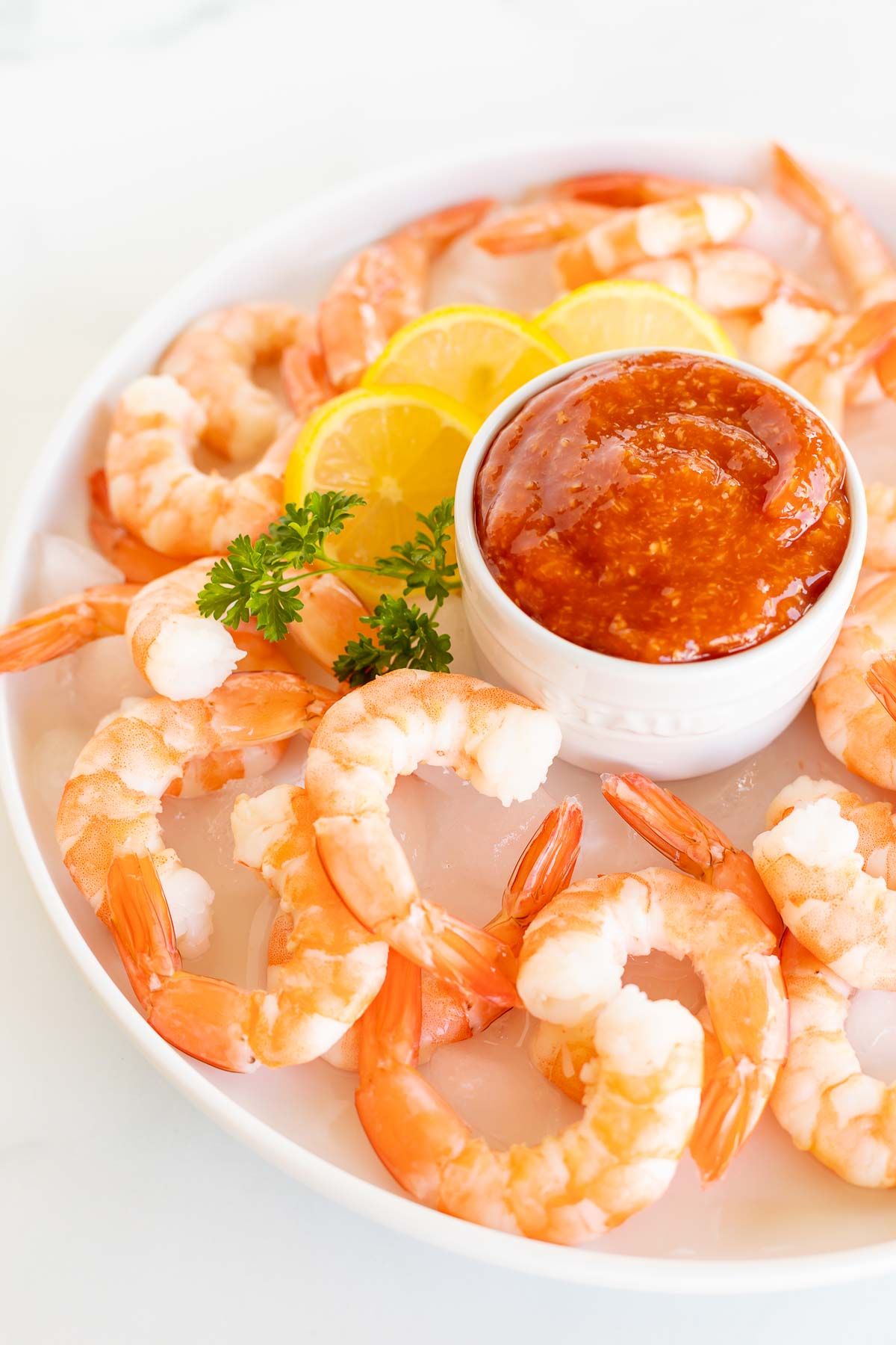 An oval platter of roasted shrimp cocktail with a homemade cocktail sauce in a white bowl.