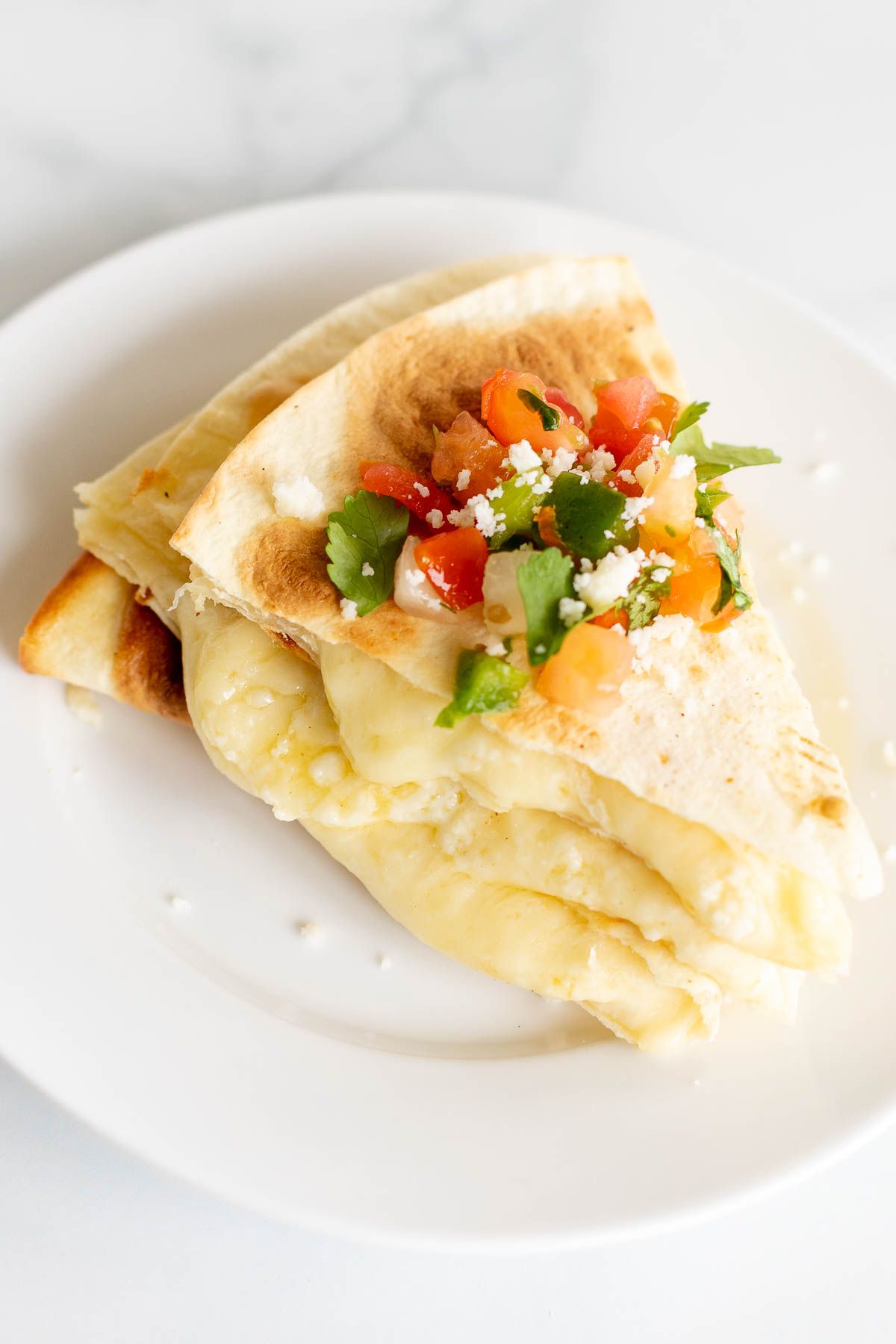 Cheese quesadilla sliced and stacked on a white plate, topped with pico de gallo