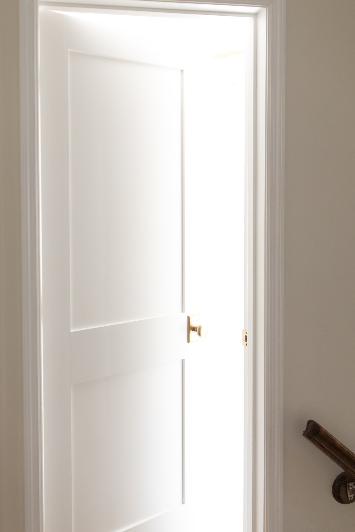 A partially open white wood door with light streaming in from the interior beyond.