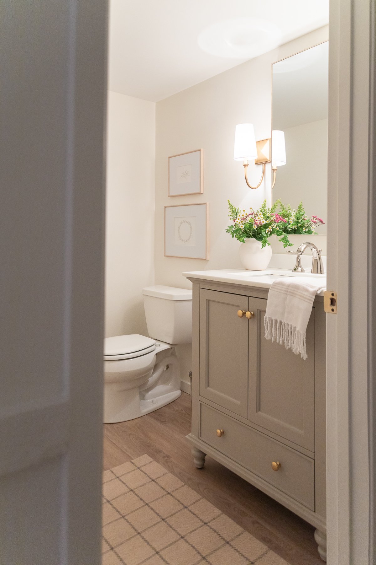 A bathroom with a sink, toilet, mirror, and neutral rugs.