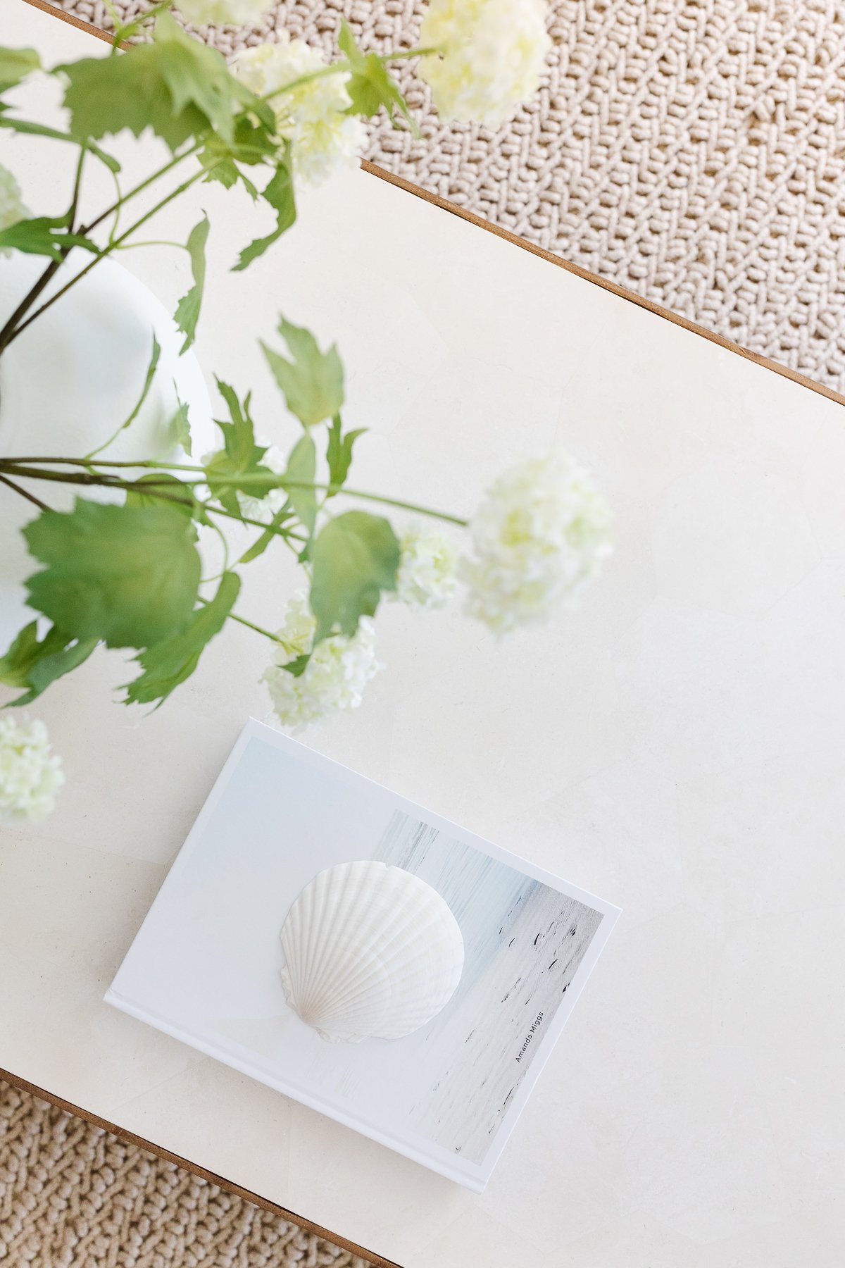 A white table with a vase of flowers on it, surrounded by neutral rugs.