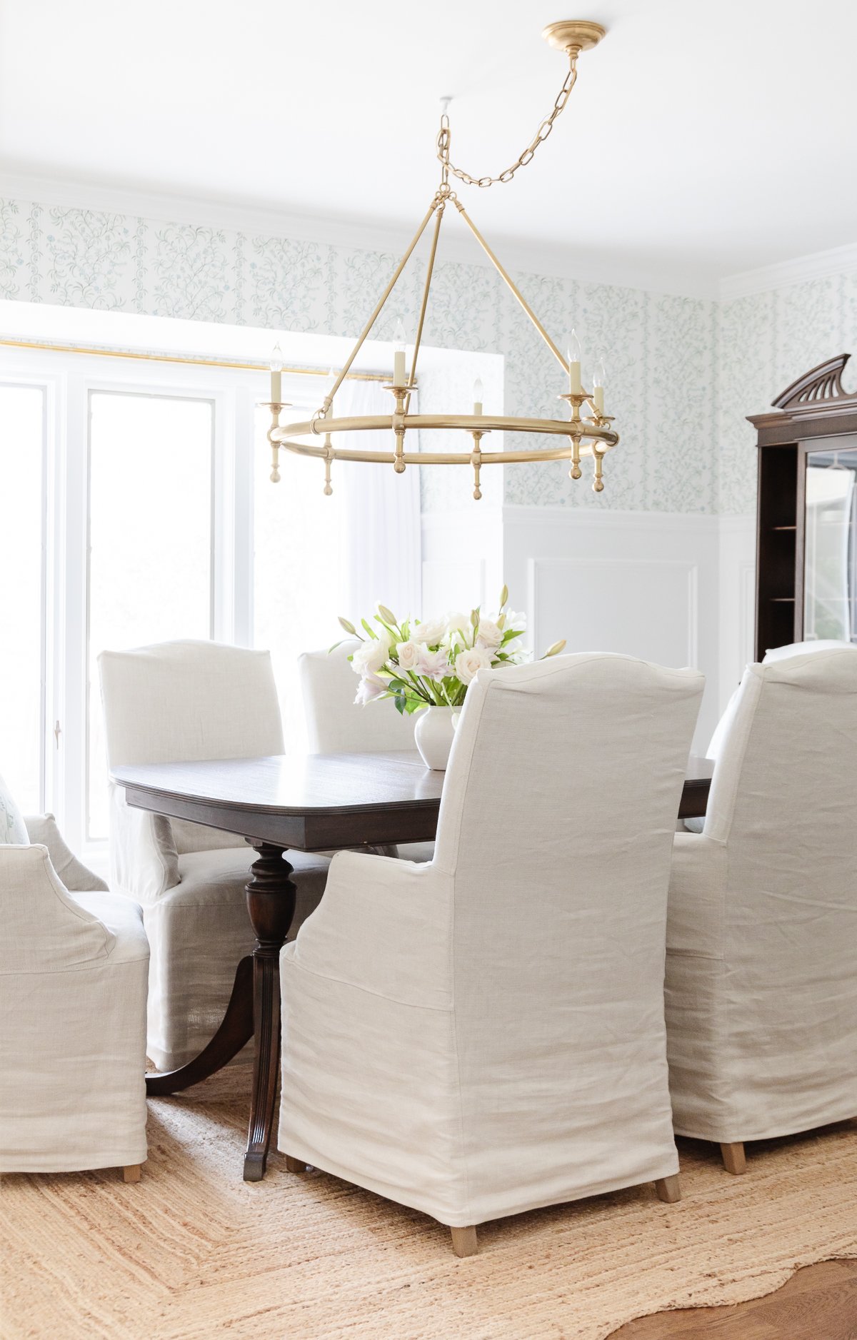 A dining room with white chairs, a chandelier, and neutral rugs.