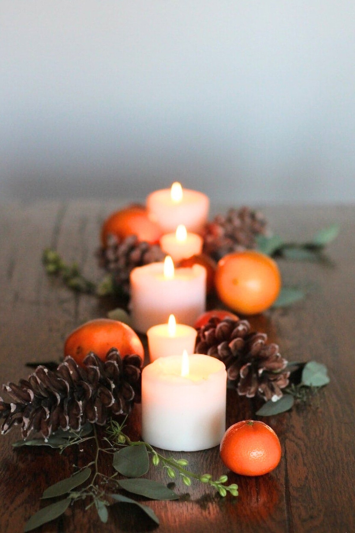 Thanksgiving table decor: A table adorned with oranges, pine cones, and candles creates a stunning centerpiece for the Thanksgiving table.