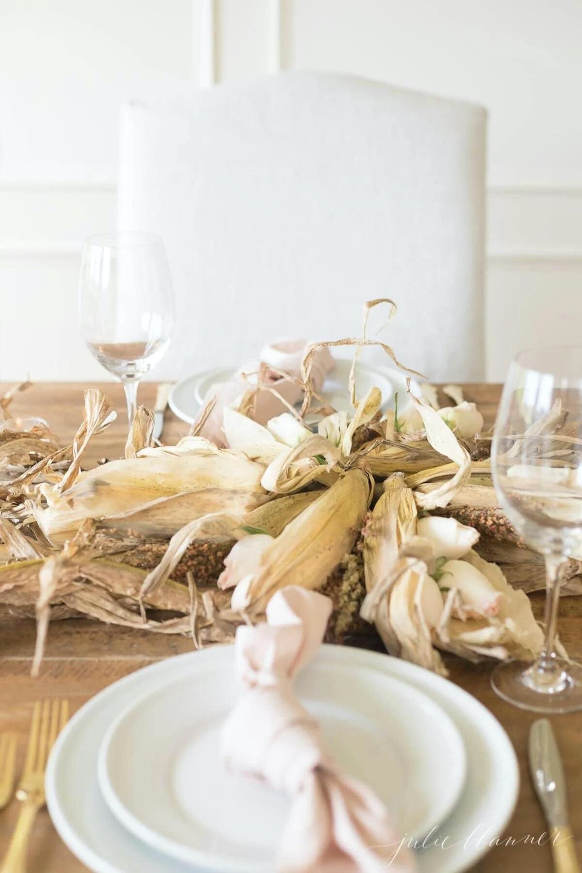 A Thanksgiving table setting with a white plate, napkin, and corn husks decorated as centerpieces.