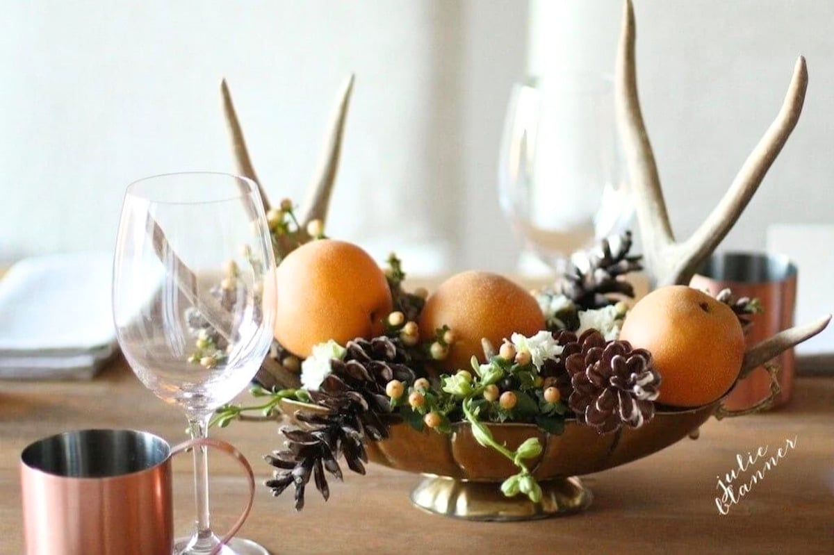 A Thanksgiving table setting adorned with oranges, grapes, and antlers.