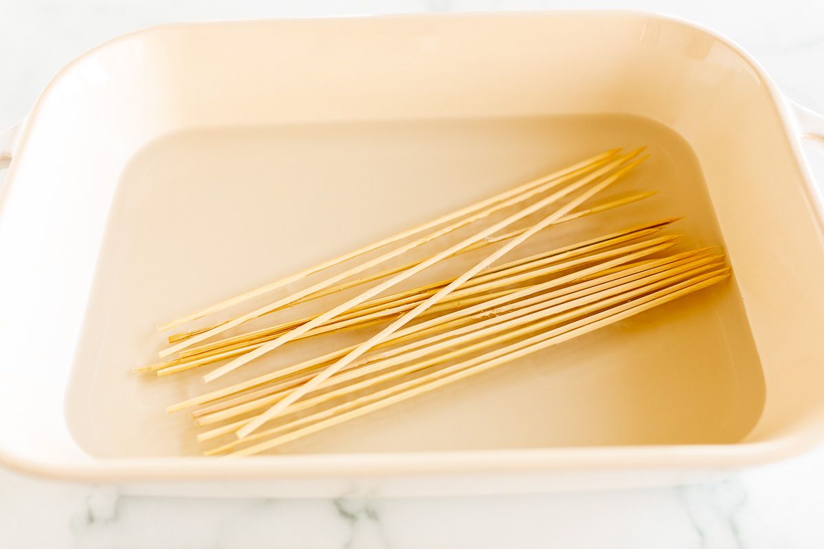 Wooden skewers soaking in water in a white baking pan