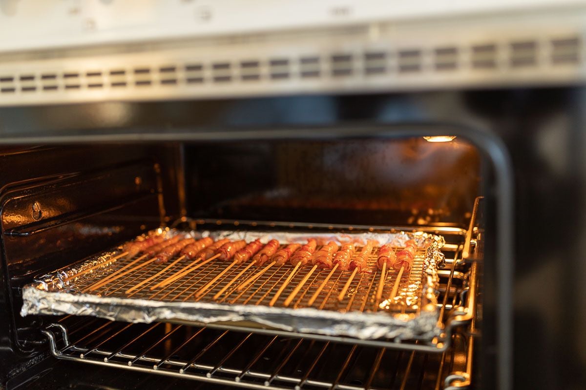 Caramel bacon on skewers, laid out on a baking sheet in the oven