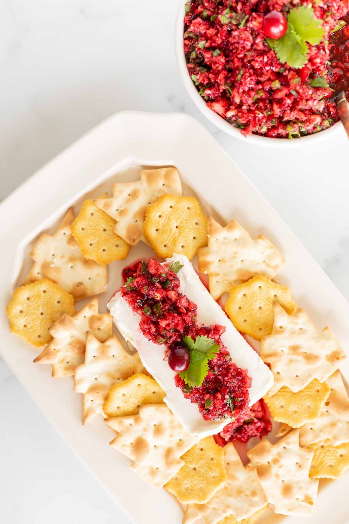 A block of cream cheese topped with cranberry salsa, surrounded by crackers for Christmas appetizers