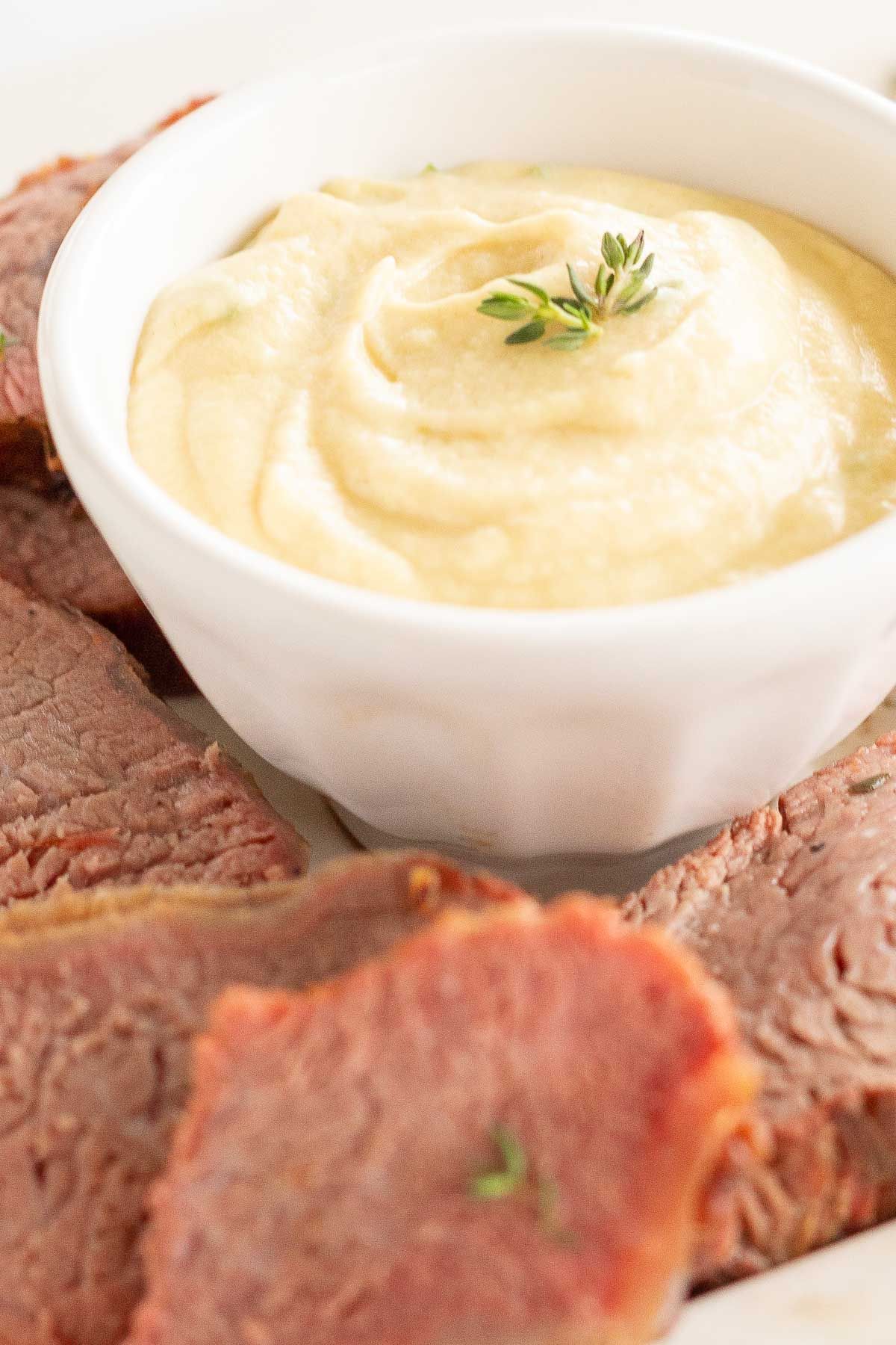 A white bowl full of Dijon sauce, surrounded by beef tenderloin.