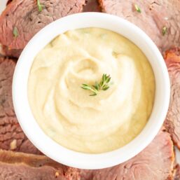 A white bowl full of Dijon sauce, surrounded by beef tenderloin.