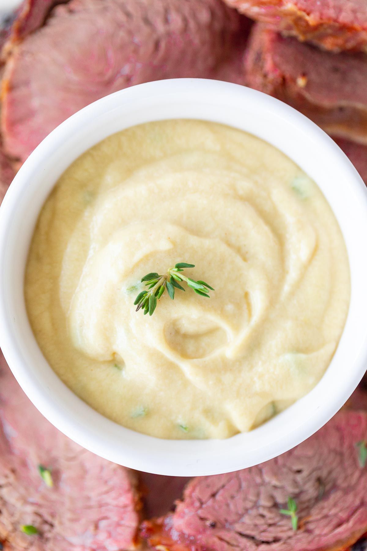 A white bowl full of Dijon mustard sauce, surrounded by beef tenderloin on a platter