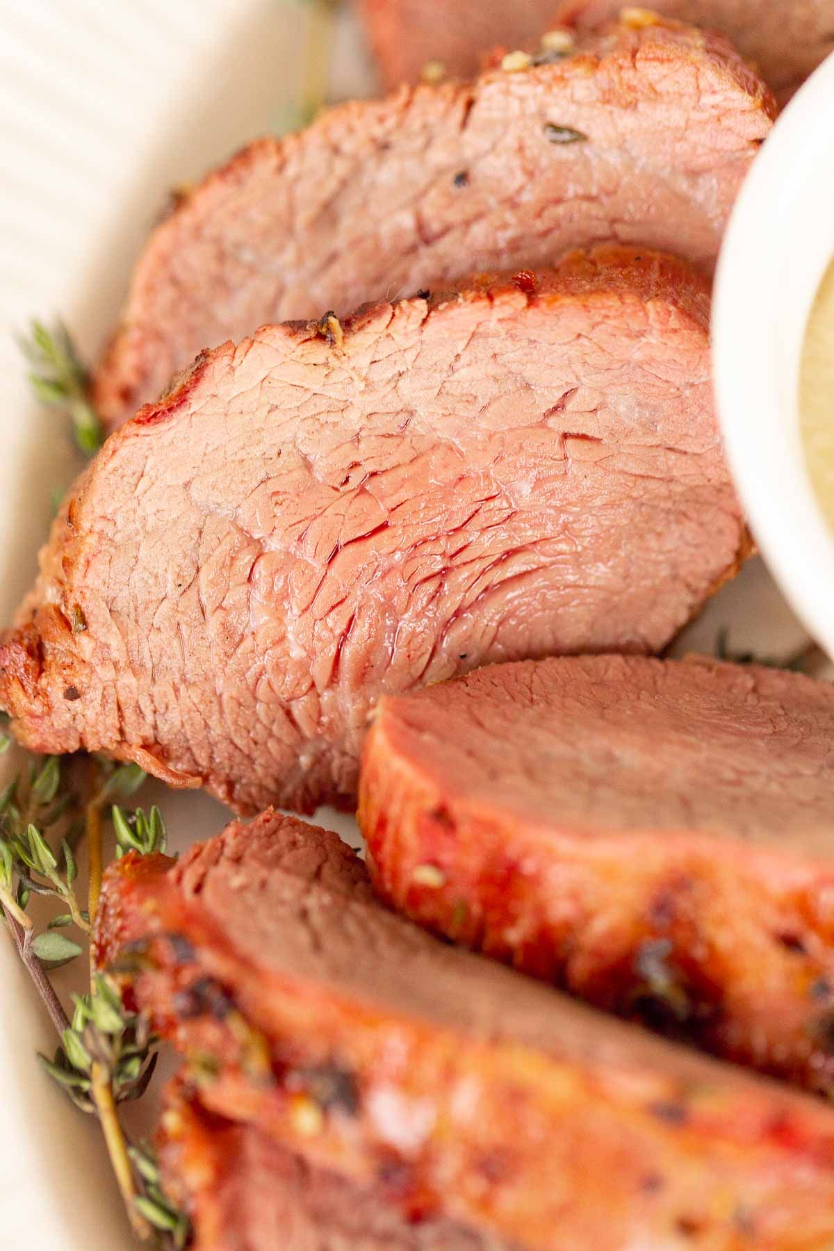 Grilled beef tenderloin on a white platter, garnished with fresh thyme.