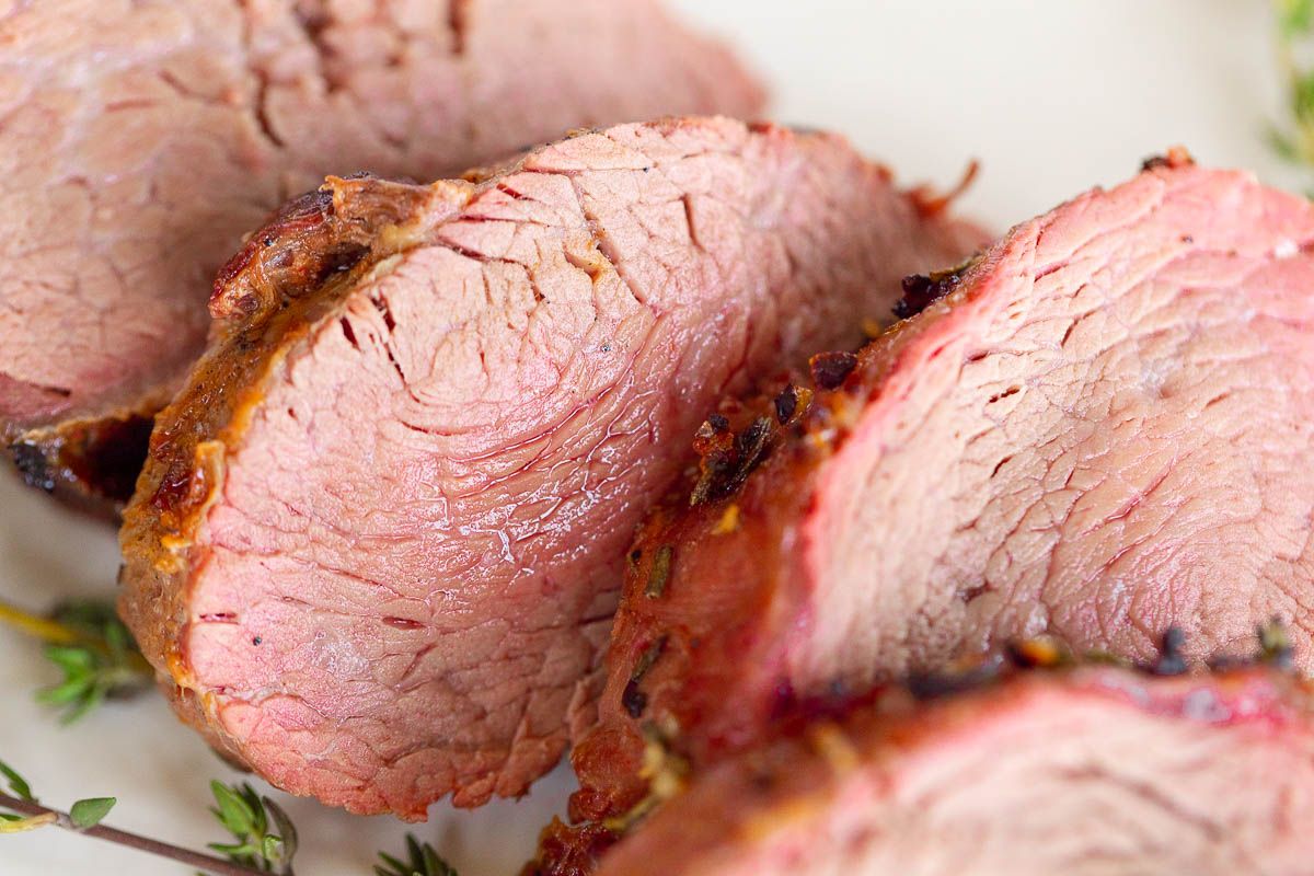 Grilled beef tenderloin on a white platter, garnished with fresh thyme.