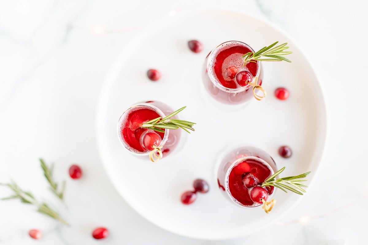 A white tray with 3 glasses full of a poinsettia cocktail